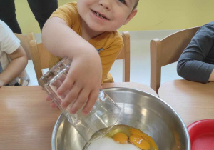 Uśmiechnięty Szymon wsypuje cukier do miski z jajkami.