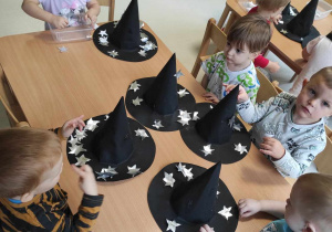 Zdjęcie dzieci siedzących przy stoliczku podczas dekorowania swoich kapeluszy.