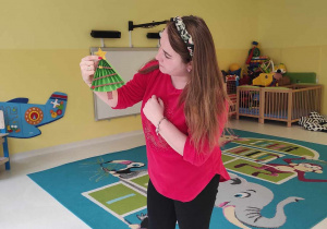 Opiekunka pokazuje dzieciom w jaki sposób mają dekorować choineczki.