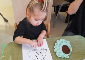 Dziewczynka rysuje igły jeża za pomocą patyczka i farby.