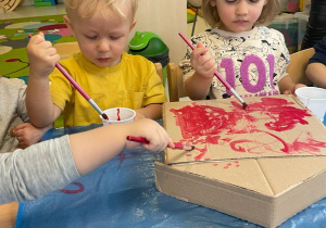 Dwoje dzieci podczas malowania na czerwono skrzynki pocztowej.