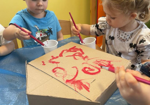 Maluchy malują czerwoną farbą skrzynkę na listy.