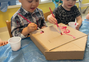 Dwóch chłopców maluje skrzynkę pocztową z tektury.