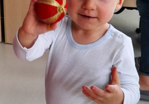 Mały chłopiec pokazuje czerwoną bombkę do zdjęcia.