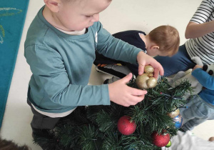 Zdjęcie Huberta wieszającego na świątecznym drzewku bombkę w kształcie złotej myszki miki.