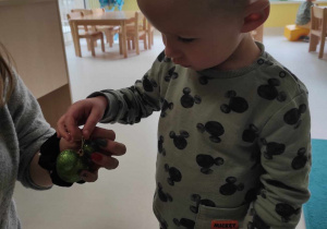 Opiekunka daje Leonowi bombkę w kształcie zielonej błyszczącej myszki miki.