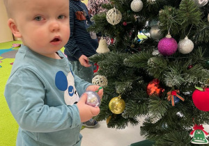 Mały chłopiec pozuje do zdjęcia przy świątecznym drzewku.