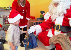 Świety Mikołaj wręcza paczkę chłopczykowi.