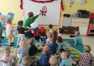Zdjęcie dzieci i opiekunki z grupy Pszczółki siedzących na dywanie podczas opowiadaniu o pisaniu listów do Świętego Mikołaja.