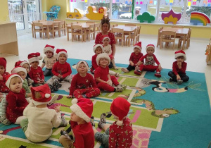 Zdjęcie dzieci i opiekunek z grupy Pszczółki siedzących na dywanie oczekujących na przyjście Świętego Mikołaja.