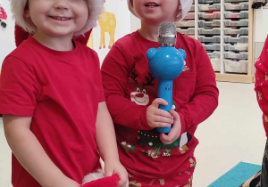 Szymon i Szymon pozują do zdjęcia trzymając w dłoni niebieski mikrofon, podczas recytowania dla Mikołaja nauczonego wiersza.