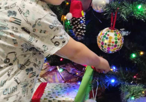 Szymon uśmiecha się podczas wieszania swojej ozdoby na świątecznym drzewku.