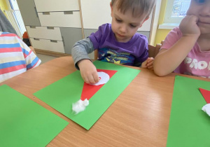 Chłopiec przykleja Mikołajowi czerwony nosek z filcu.
