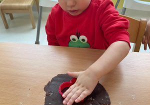 Mały chłopiec próbuje wyciąć ciasteczko w kształcie serduszka.
