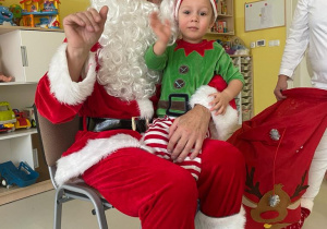 Chłopiec macha do zdjęcia na kolanach u Świętego Mikołaja.