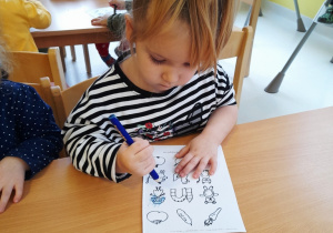 Dziewczynka maluje lalkę na kartce.