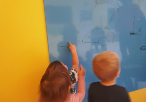 Mała dziewczynka pokazuje palcem na obrazek namalowany na tablicy.