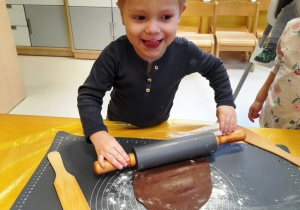 Uśmiechnięty chłopiec wałkuje ciasto.