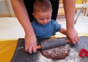 Mały chłopczyk z pomocą opiekunki wałkuje piernikowe ciasto.
