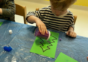 Chłopiec sypie fioletowy brokat na papierową choinkę.