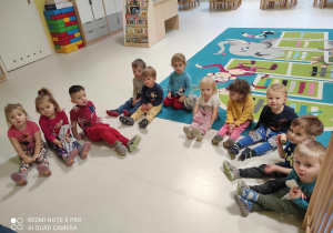 Zdjęcie dzieci z grupy Pszczółki siedzących na podłodze i przygotowujących się do zajęć pt. ,,Rękawiczkowa segregacja''.