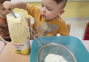 Szymon samodzielnie nabiera łyżką mąkę.