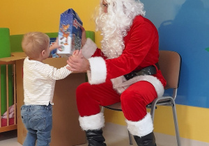 Mikołaj podaje prezent małemu chłopczykowi.