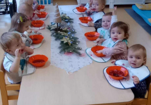 Zdjęcie dzieci siedzących przy wigilijnym stole, podczas kosztowania świątecznego barszczyku.