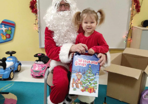 Uśmiechnięta Iga pozuje do zdjęcia razem ze swoim prezentem siedząc na kolanach Świętego Mikołaja.