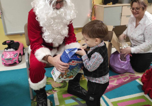 Tymoteusz odbiera od Świętego Mikołaja swój upominek zapakowany w niebieskie świąteczne pudełeczko.