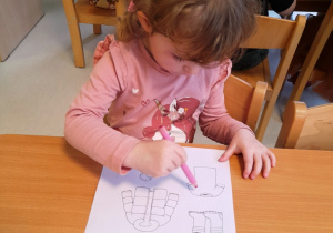 Dziewczynka maluje wydrukowane na kartce ubranka na różówo.