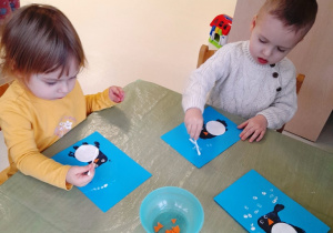 Dwoje dzieci przykleja kolejne elementy do swojego pingwinka.