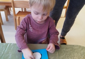 Chłopczyk nakleja biały wacik na odciśniętą dłoń na kartce.