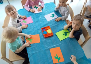 Dzieci z grupy Biedroneczki siedząc przy stole, czekają na malowanie farbami.