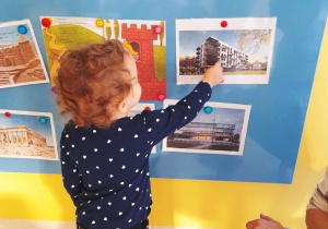 Dziewczynka wskazuje na ilustrację przedstawiającą blok mieszkalny.