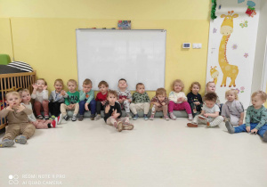 Zdjęcie dzieci z grupy Pszczółki siedzących na zwiniętym dywanie, przygotowujących się do zajęć muzyczno - ruchowych pt. ,,PORZĄDKOWE KÓŁECZKA''.