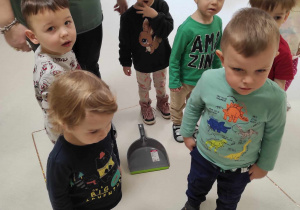 Zdjęcie dzieci stojących w wyklejonym kwadracie, z przyklejoną na taśmę klejącą szarą szufelką.