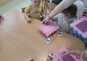Zdjęcie opiekunki rozdającej dzieciom kolorowe wykonane własnoręcznie ramki.