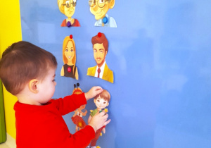 Maluch przykleja na tablicy ilustrację przedstawuającą chłopczyka.
