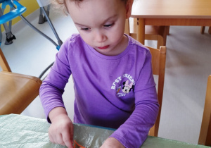 Dziewczynka nakleja kawałki wełny na papierowe koło.
