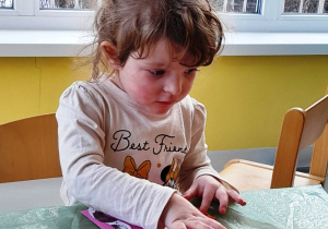 Dziewczynka nakleja na kartkę szablon kota oraz wełniane kółeczko.