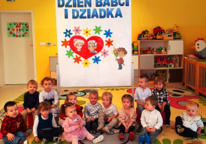 Pamiątkowa fotografia dzieci z grupy Biedroneczki na tle ścianki z okazji Dnia Babci i Dziadka.