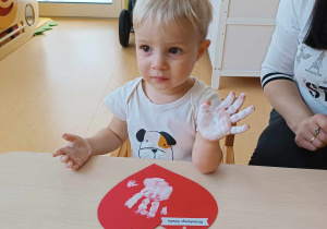 Antoni pokazuje opiekunce robiącej zdjęcie pomalowaną białą farbą dłoń.