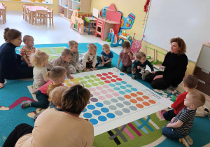 Zdjęcie Pani prowadzącej zajęcia, która tłumaczy dzieciom i opiekunkom z grupy Pszczółki na czym polegać będą zajęcia z kodowania.