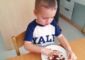 Chłopiec maluje na talerzyku za pomocą czekoladowego musu.