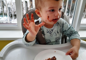 Chłopiec macha do zdjęcia dłonią wysmarowaną czekoladą.