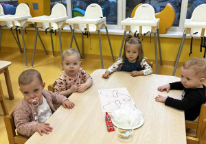 Zdjęcie dzieci z grupy Motylki siedzących przy stoliczku i przygotowujących się do pracy plastycznej pt. ,,ZIMOWE RĘKAWICZKI''.