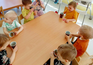 Dzieci z grupy Biedroneczki siedząc przy stoliku degustują wcześniej wykonany sok.