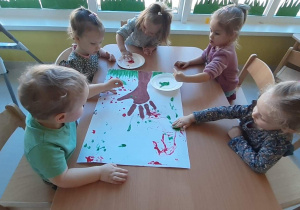Fotografia dzieci siedzących przy stole podczas malowania farbami.