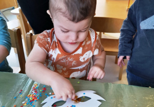 Chłopiec posypuje szablon maski kolorowym konfetti.